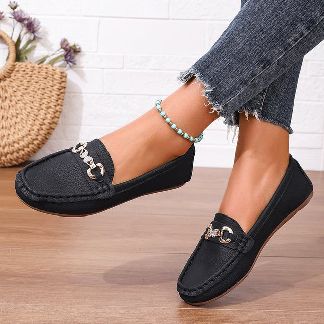 Black loafers with gold accents worn by a person on a wooden floor.