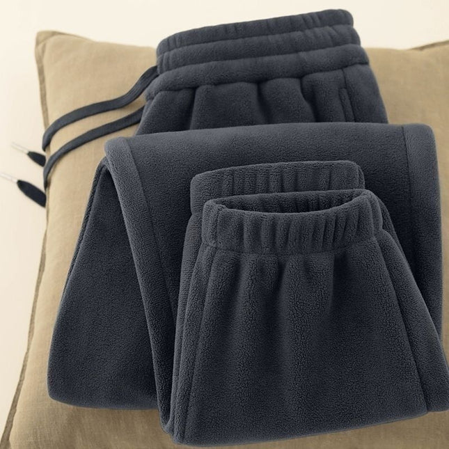 Folded dark gray fleece pants on a beige pillow