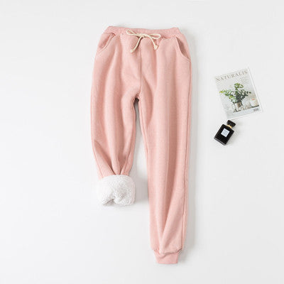 Pink sweatpants on a white background with a small plant and bottle.