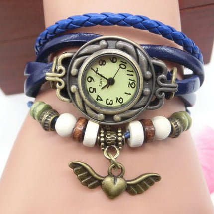 Multicolored bracelet with a vintage-style watch face and winged heart charm on a wrist.