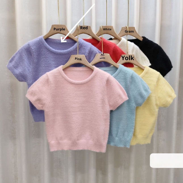Colorful baby sweaters on hangers with labeled colors against a neutral background