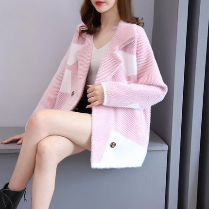 Person wearing a pink cardigan with white accents sitting on a gray surface.