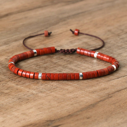Adjustable beaded bracelet with red spacer beads and silver accents on a wooden background.
