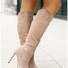 Beige knee-high boots worn with a blue polka dot dress on a blurred background