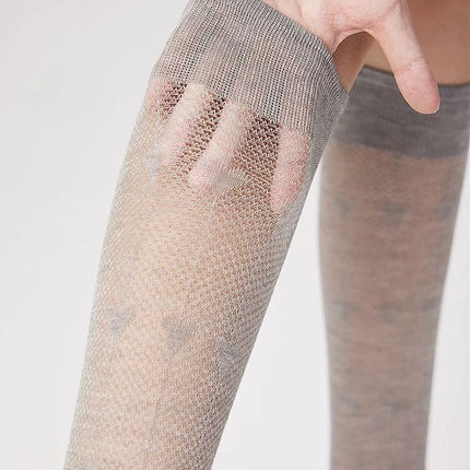 Close-up of a person wearing fishnet stockings with a plain background