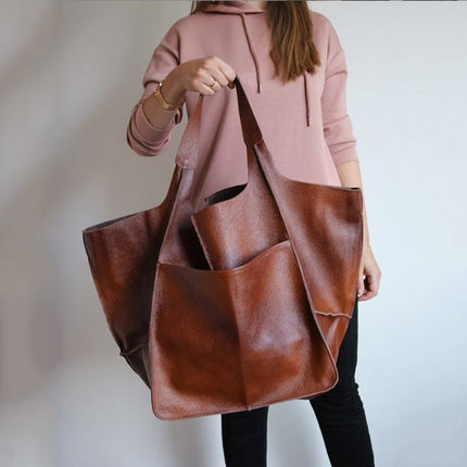 Person holding a brown leather tote bag against a neutral background