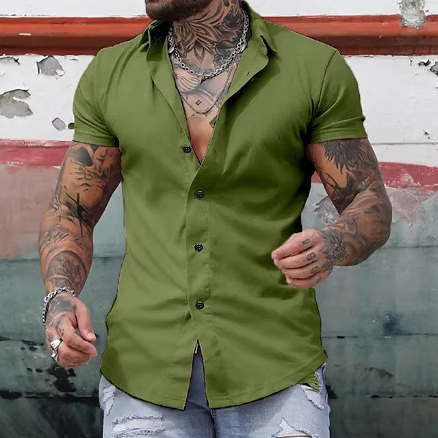 Man wearing a green button-up shirt with tattoos visible, standing against a rustic wall.