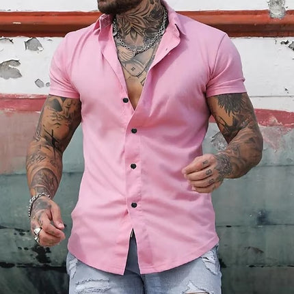 Man wearing a pink short-sleeve shirt with tattoos visible on his arms against a rustic background.