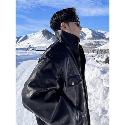 Person wearing a black leather jacket standing in a snowy landscape with mountains in the background