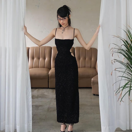 Woman in a black dress standing between two white curtains in a room with a beige sofa.