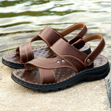 Brown sandals with black soles on a stone surface near water.