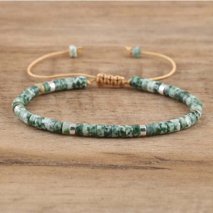 Hand-woven natural stone adjustable bracelet featuring green jade beads with silver accents on a wooden surface.