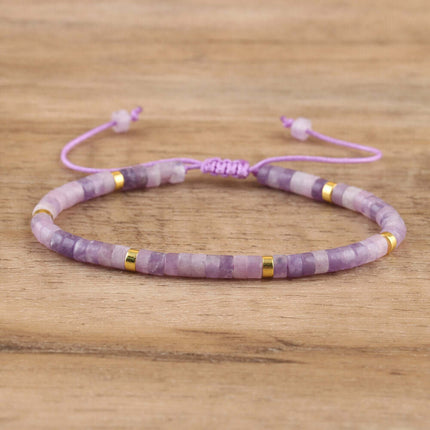 Adjustable purple beaded bracelet with gold accents on a wooden background, featuring a hand-woven design.