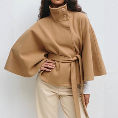 Person wearing a brown cape over a white shirt and beige pants on a white background
