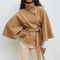 Person wearing a brown cape over a white shirt and beige pants on a white background