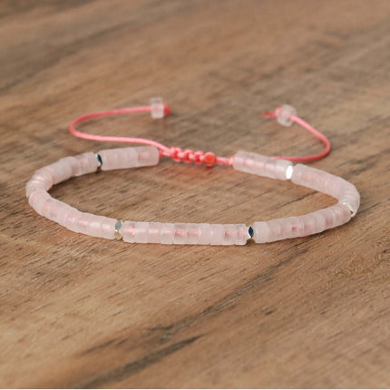 Adjustable pink beaded bracelet on wooden surface, featuring natural stone spacers and a simple woven design.