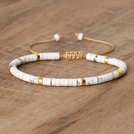 Adjustable women's beaded bracelet with white and gold accents on a wooden surface.