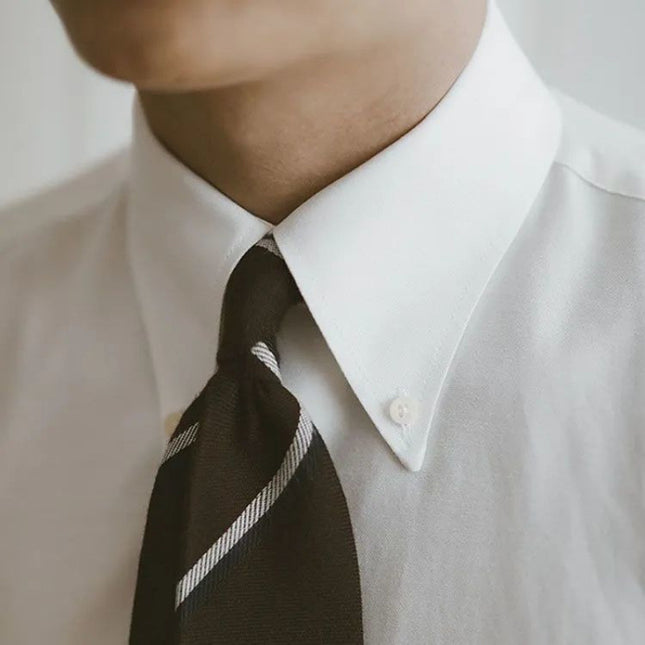 Close-up of a person wearing a white shirt and black striped tie.
