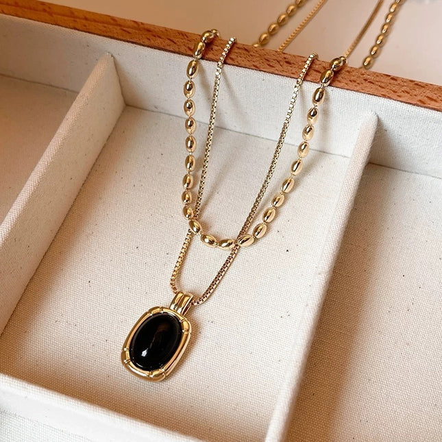 Gold necklace with a black pendant on a beige fabric background
