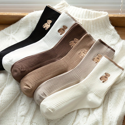 Set of four pairs of socks in black, white, brown, and beige with teddy bear designs on a textured surface.