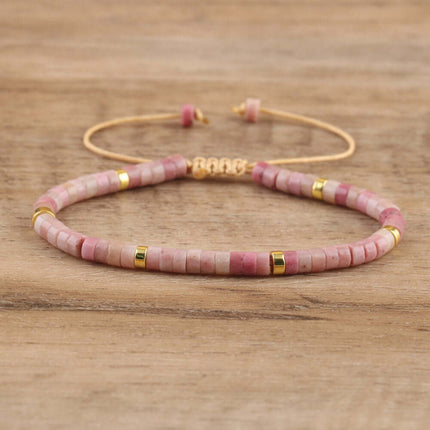 Women's pink natural stone beaded bracelet with gold accents on a wooden surface.