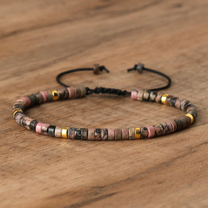 Adjustable women's bracelet featuring natural stone spacer beads in pink, gold, and earthy tones on a wooden background.