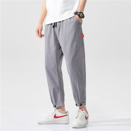 Person wearing gray jogger pants with a white shirt and white sneakers on a light gray background