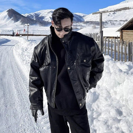 Person wearing a black leather jacket and sunglasses standing in a snowy landscape with mountains in the background.