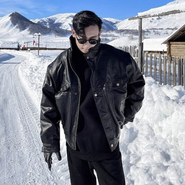 Person wearing a black leather jacket and sunglasses standing in a snowy landscape with mountains in the background.