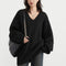 Person wearing a black oversized sweater holding a black bag on a light gray background