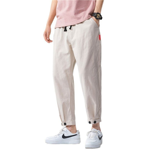 Person wearing beige pants with black accents and white sneakers on a white background