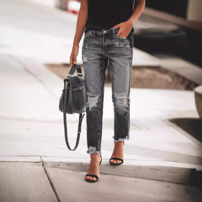 Person wearing distressed gray jeans and black sandals, holding a black handbag.