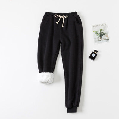 Black sweatpants on a white background with a small plant and bottle.