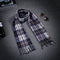 Plaid scarf on a dark surface with sunglasses and a book in the background