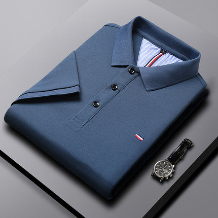Folded blue polo shirt with a watch on a gray surface