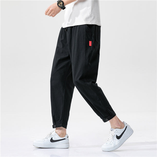 Person wearing black pants with a red tag and white sneakers on a light gray background